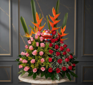 Arreglo floral de cumpleaños con rosas rojas y rosas, aves del paraíso naranjas, follaje verde y globo redondo con texto feliz cumpleaños sobre mesa de mármol