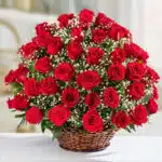 Ramo grande de rosas rojas frescas con paniculata blanca en una canasta de mimbre sobre superficie blanca