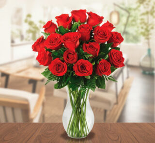 Arreglo de rosas rojas frescas en un jarrón de cristal transparente colocado sobre una mesa de madera, con fondo de sala desenfocado