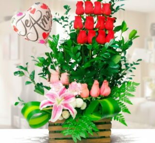 Arreglo floral en base de madera con rosas rojas verticales, rosas rosadas, lirio rosa, follaje verde y globo metálico en forma de corazón con la frase Te amo