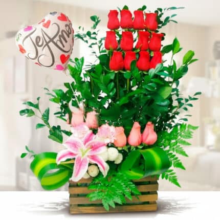 Arreglo floral en base de madera con rosas rojas verticales, rosas rosadas, lirio rosa, follaje verde y globo metálico en forma de corazón con la frase Te amo