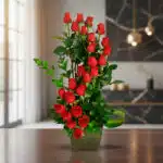 Arreglo floral alto de rosas rojas con follaje verde en florero cuadrado verde sobre mesa de madera en sala moderna desenfocada
