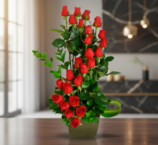 Arreglo floral alto de rosas rojas con follaje verde en florero cuadrado verde sobre mesa de madera en sala moderna desenfocada