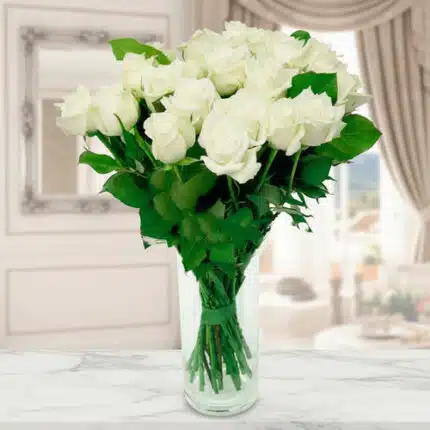 Ramo de rosas blancas frescas en un jarrón de cristal transparente sobre encimera de mármol, con fondo de salón elegante desenfocado