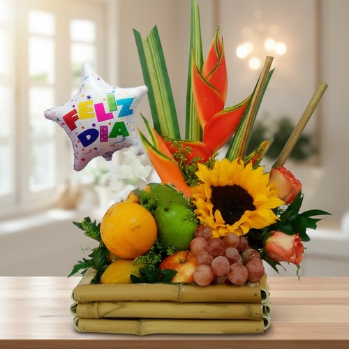 Arreglo de frutas y flores con globo Feliz Día Arreglo de frutas variadas con girasol, heliconias y globo metálico con texto Feliz Día sobre base de bambú en interior iluminado