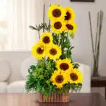 arreglo vertical de girasoles amarillos frescos con follaje verde en maceta de bambú sobre mesa en sala de estar luminosa