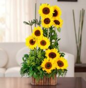 arreglo vertical de girasoles amarillos frescos con follaje verde en maceta de bambú sobre mesa en sala de estar luminosa