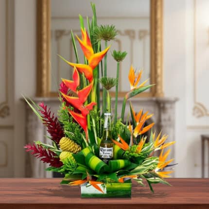 Arreglo floral tropical con heliconias naranjas, follaje verde y una botella de cerveza en el centro, sobre mesa de madera en interior elegante