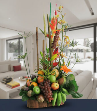Centro de mesa con frutas frescas y flores tropicales de colores sobre base de madera en una sala de estar moderna y luminosa