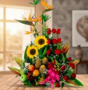 Centro de mesa con girasoles, rosas rojas, aves del paraíso y frutas tropicales sobre una mesa de madera en interior