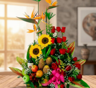 Centro de mesa con girasoles, rosas rojas, aves del paraíso y frutas tropicales sobre una mesa de madera en interior