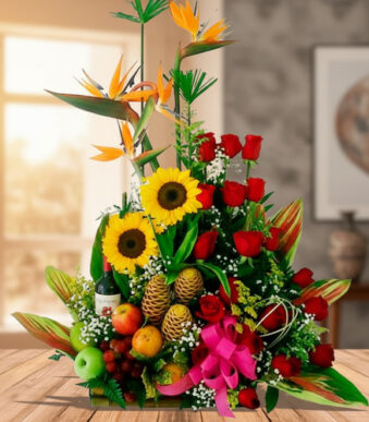 Centro de mesa con girasoles, rosas rojas, aves del paraíso y frutas tropicales sobre una mesa de madera en interior