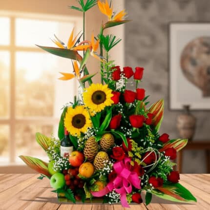 Centro de mesa con girasoles, rosas rojas, aves del paraíso y frutas tropicales sobre una mesa de madera en interior