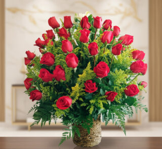 Arreglo floral de rosas rojas con follaje verde en canasta de mimbre sobre mesa de madera