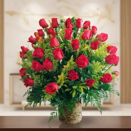 Arreglo floral de rosas rojas con follaje verde en canasta de mimbre sobre mesa de madera