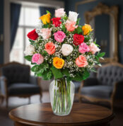 Arreglo floral de rosas rojas, rosas, blancas, amarillas y naranjas con paniculata en un jarrón de cristal sobre una mesa de madera en una sala elegante