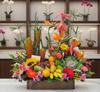 Centro de mesa con frutas y flores tropicales de colores vivos sobre una mesa de mármol en interior
