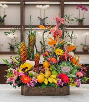 Centro de mesa con frutas y flores tropicales de colores vivos sobre una mesa de mármol en interior