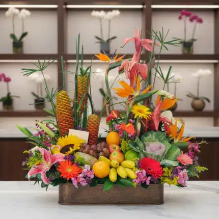 Centro de mesa con frutas y flores tropicales de colores vivos sobre una mesa de mármol en interior