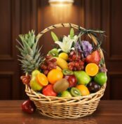 Cesta de mimbre llena de frutas frescas como piñas, naranjas, manzanas, uvas, kiwis y peras sobre una mesa de madera con fondo marrón