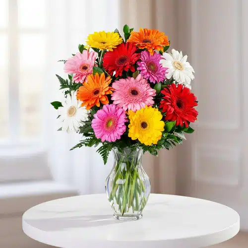 Ramo de gerberas de colores en jarrón de cristal Ramo de gerberas rojas, rosas, naranjas, amarillas y blancas en un jarrón de cristal transparente sobre una mesa redonda blanca