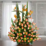 Arreglo floral grande con rosas naranjas y flores aves del paraíso sobre una mesa en interior