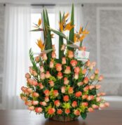 Arreglo floral grande con rosas naranjas y flores aves del paraíso sobre una mesa en interior