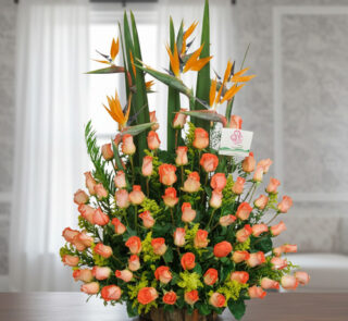 Arreglo floral grande con rosas naranjas y flores aves del paraíso sobre una mesa en interior