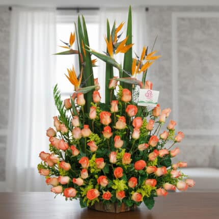 Arreglo floral grande con rosas naranjas y flores aves del paraíso sobre una mesa en interior