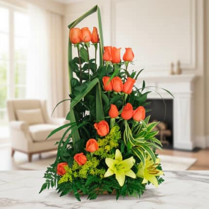 Arreglo floral vertical con rosas naranjas, lirios amarillos y follaje verde colocado sobre una mesa de mármol en una sala luminosa