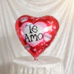 Globo metálico rojo en forma de corazón con la frase Te Amo sobre fondo de tela blanca
