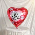 Globo metálico rojo en forma de corazón con la frase Te Amo sobre fondo de tela blanca