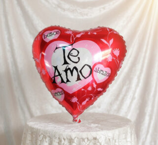 Globo metálico rojo en forma de corazón con la frase Te Amo sobre fondo de tela blanca