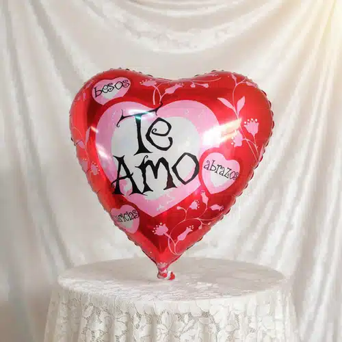 Globo metálico rojo en forma de corazón con la frase Te Amo sobre fondo de tela blanca