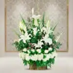 Arreglo floral elegante con lirios blancos, rosas blancas y follaje verde en base de bambú sobre fondo desenfocado