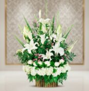 Arreglo floral elegante con lirios blancos, rosas blancas y follaje verde en base de bambú sobre fondo desenfocado
