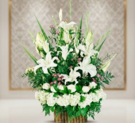 Arreglo floral elegante con lirios blancos, rosas blancas y follaje verde en base de bambú sobre fondo desenfocado