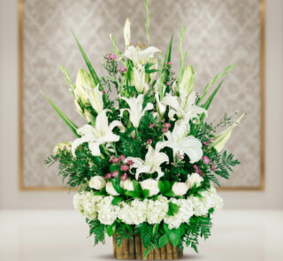 Arreglo floral elegante con lirios blancos, rosas blancas y follaje verde en base de bambú sobre fondo desenfocado