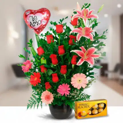 Arreglo floral en maceta negra con rosas rojas, lirios rosados, gerberas y globo rojo en forma de corazón con texto Te amo junto a caja de chocolates Ferrero Rocher