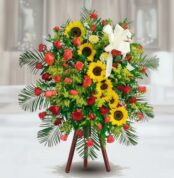 Arreglo funerario de pie con girasoles amarillos, rosas rojas y follaje verde sobre caballete de madera