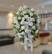 Arreglo floral grande de flores blancas con lazos y follaje verde sobre caballete de madera en una sala interior desenfocada