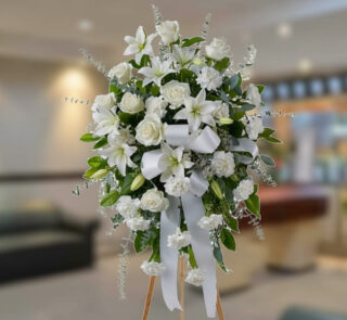 Arreglo floral grande de flores blancas con lazos y follaje verde sobre caballete de madera en una sala interior desenfocada