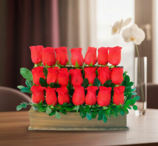 Arreglo de varias rosas rojas en filas dentro de una caja de madera con hojas verdes, colocado sobre una mesa en interior