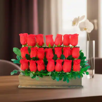 Arreglo de varias rosas rojas en filas dentro de una caja de madera con hojas verdes, colocado sobre una mesa en interior