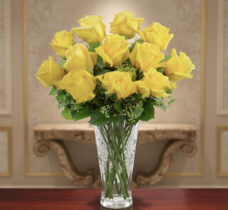 Ramo de rosas amarillas frescas en un jarrón de cristal tallado sobre una mesa de madera, con fondo interior elegante desenfocado