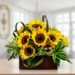 Arreglo floral de girasoles amarillos con follaje verde en una cesta cuadrada de madera sobre una mesa, con fondo de interior desenfocado