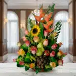 Arreglo floral con rosas de colores, girasol, heliconias y frutas como uvas, peras y manzanas sobre una mesa de mármol en interior elegante