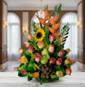 Arreglo floral con rosas de colores, girasol, heliconias y frutas como uvas, peras y manzanas sobre una mesa de mármol en interior elegante