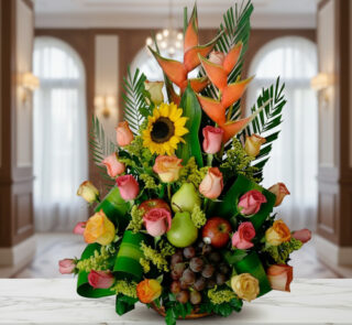 Arreglo floral con rosas de colores, girasol, heliconias y frutas como uvas, peras y manzanas sobre una mesa de mármol en interior elegante