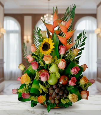 Arreglo floral con rosas de colores, girasol, heliconias y frutas como uvas, peras y manzanas sobre una mesa de mármol en interior elegante
